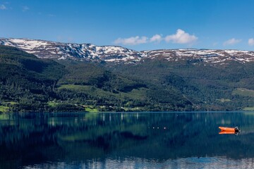 Obraz premium Serene lake with an orange boat and snow-capped mountains in Norway under a clear blue sky