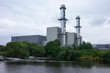 Obraz premium Industrial power plant with two tall chimneys near a river on a cloudy day.