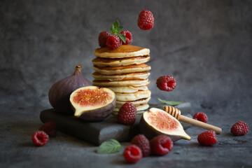 Pancakes with raspberries and figs on a dark background.