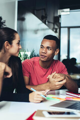 Diverse male and female colleagues communicating about ideas for startup project sitting at desktop with modern digital technology, skilled group of students spending time for studying together