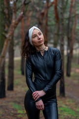 Beautiful young woman in black leather overalls posing in autumn forest