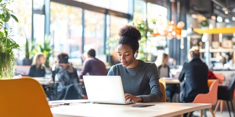 A person with a hearing aid working in a modern co-working space, focusing on a laptop, surrounded by others immersed in work, the bright open-plan office bustling with a