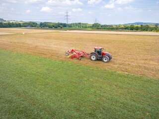 Fototapeta premium Aerial view of a red tractor plowing the field on a sunny summer day
