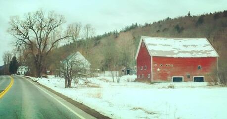 Rural winter landscape featuring a red barn and snow-covered ground along a winding road