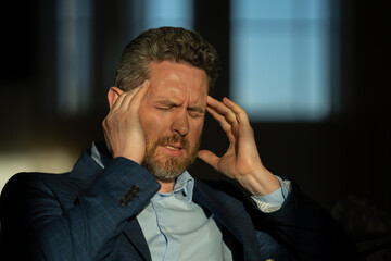 Tired exhausted man suffering from headache. Overworked burnout man feeling migraine head strain. Bored business man has office syndrome. Office worker, manager or freelancer having a headache.