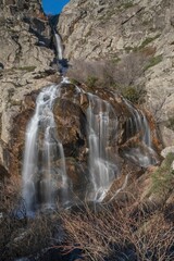 Waterfall cascading down rocky cliffs under a clear blue sky.