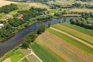 Drone aerial perspective of a river flowing through the Polish countryside in summer, surrounded by green foliage.