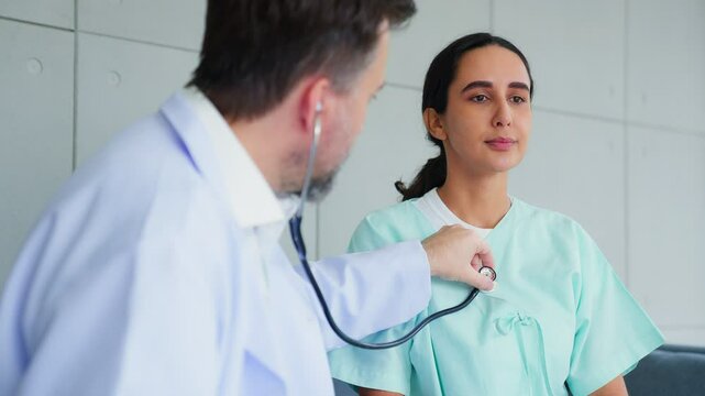 Older man cardiologist in white coat using phonendoscope listening heartbeat of woman patient at medical annual  health check up during meeting in clinic or hospital office. Healthcare, medicine.