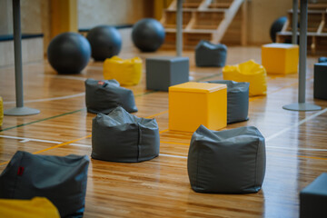Obraz premium Valmiera, Latvia - April 26, 2024 - A gym setup featuring gray and yellow bean bags, fitness balls, and cubes on a polished wooden floor, arranged for an event or activity.