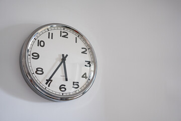 Round analog clock hanging on white wall. Shows clean and modern style with functional design.