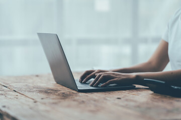 Fototapeta premium Focused Productivity: Hands typing on a laptop, bathed in natural light, on a rustic wooden desk, evoking a sense of quiet concentration and remote work efficiency. 