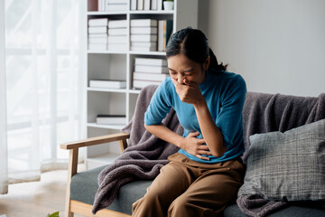 Woman in the living room at home has stomach ache and press hands to stomach due to menstrual cramps period cramps splenomegaly  food poisoning excess gas or acid and vomit