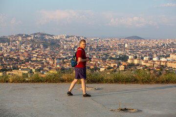 Man checks phone on hilltop path, vast cityscape sprawls below in golden light, urban adventure...