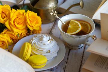 On the white table there is hot tea, cakes and delicate roses.