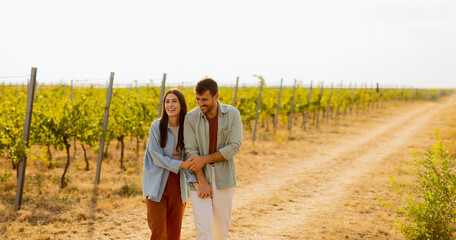 A joyful couple laughing together in a sunlit vineyard during a warm afternoon, surrounded by lush grapevines and a rustic path