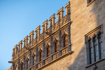 The intricate stonework and beautifully crafted windows of an impressive historic structure facade basking in warm sunlight in Valencia, Spain