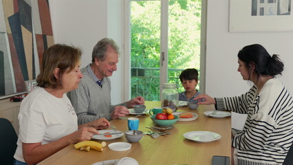 Four family members having a meal around a table, engaging in lively conversation, in a warm, inviting home atmosphere with a large window in the background allowing natural light