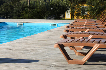 Empty sun loungers on wooden deck near outdoor swimming pool