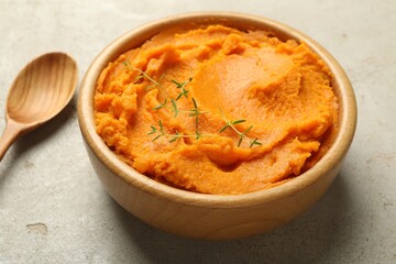 Tasty mashed sweet potato and thyme in bowl on grey textured table, closeup