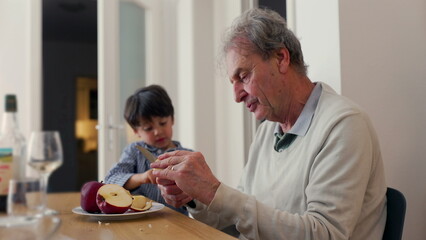 Grandfather and grandson at a dining table, sharing an apple. scene emphasizes family bonding and togetherness during a simple meal in a cozy home environment