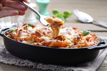 Woman eating delicious al forno pasta at wooden table, closeup