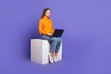 Photo of cheerful youngster girl in orange turtleneck and jeans using laptop at lecture room sit...