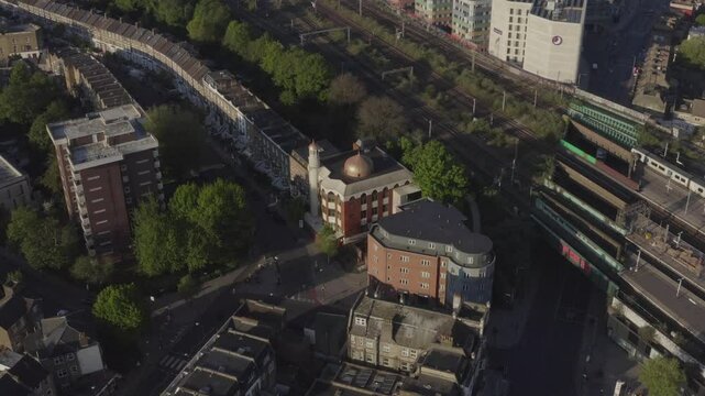 Aerial shot circling Finsbury Park mosque with railway and tower blocks in the background and Londoners roaming in the streets