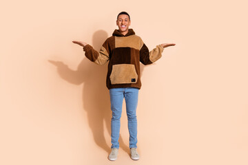 Photo of optimistc guy with stylish haircut dressed hoodie arms demonstrate objects empty space isolated on beige color background