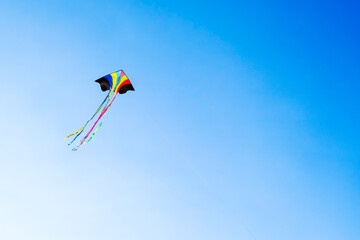colorful kite with long flowing tails flies high in a clear blue sky, creating a sense of freedom and fun.