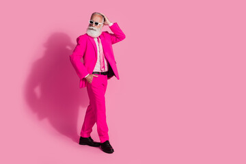 Full body photo of elderly white hair santa man walk touch head hair sunglass wear stylish pink suit isolated over pastel color background