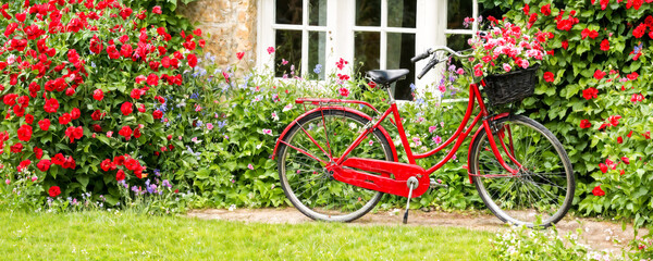 A bright red bicycle rests by a quaint cottage adorned with blooming flowers, capturing the essence of springtime in a serene countryside setting.