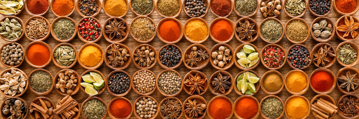 Fototapeta premium A colorful array of spices fills wooden bowls, displaying rich textures and vibrant hues. Fragrant cinnamon sticks and a variety of seeds create an inviting atmosphere in a lively marketplace.