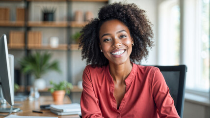 A black woman with curly hair sits comfortably in an office chair, smiling warmly at the camera. Sunlight pours into the workspace, highlighting her joyful demeanor and the contemporary office decor.
