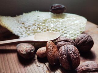Honey in honeycomb with wooden spoon, almonds and walnuts in shell