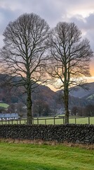 The English countryside is bathed in soft orange light during sunset, showcasing rolling hills and silhouetted trees with visible brushstrokes for added depth