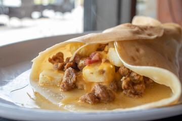 A Breakfast Crepe Pancake with Sausage, Egg, and Cheese Near a Window