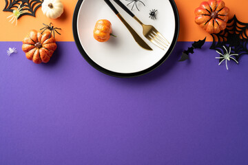 Top view of a Halloween-themed table setting with pumpkins, cutlery, and decorative spiders on a vibrant orange and purple background