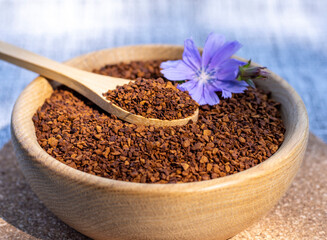 Ground chicory root on a wooden spoon and chicory flowers on a rustic wooden background. Alternative medicine. Healthy drinks. chicory drink