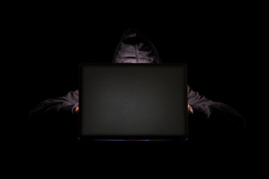 A person in a dark room using a laptop, internet phishing, hacking, data security threats, data breach, cyber security concept