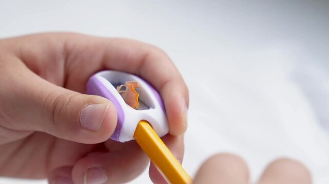 Children's hands sharpening a yellow pencil with a sharpener