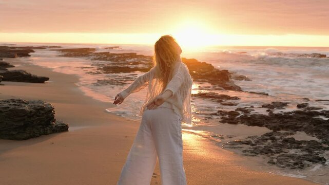 A modern dancer stretches her arms elegantly by the sea during sunset, embodying fluidity and freedom.