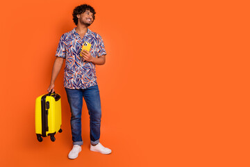 Full size photo of nice young man look empty space hold suitcase device wear trendy colorful outfit isolated on orange color background