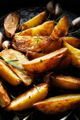 Close up of  potato wedges  seasoned with aromatic herbs and garlic on a dark background
