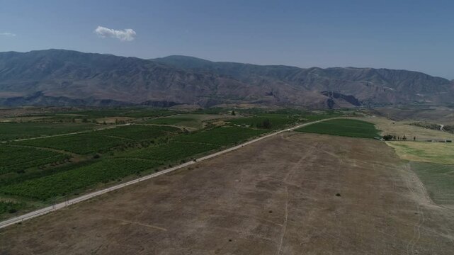 Drone pullout of a vast rural field with a road, and mountain with blue sky in the background