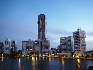 Fototapeta premium Cityscape of modern high-rise buildings reflected in a body of water at dusk with a clear blue sky