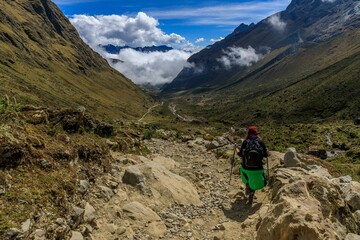 Hiker trekking through a scenic mountain valley with a clear blue sky and clouds in the background