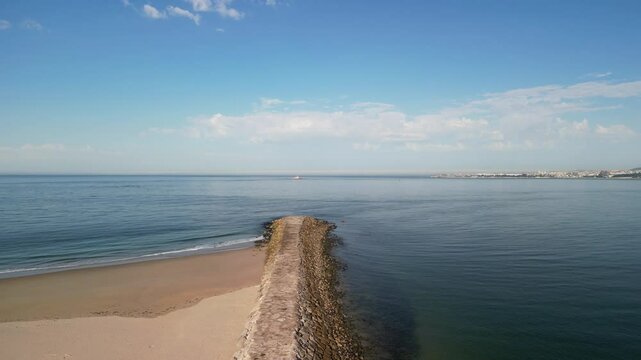 Aerial view of Atlantic Ocean with empty sandy beach and stone breakwater on a sunny day