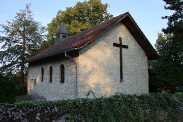 Quaint church with a cross on its wall, surrounded by lush greenery and bathed in soft sunlight