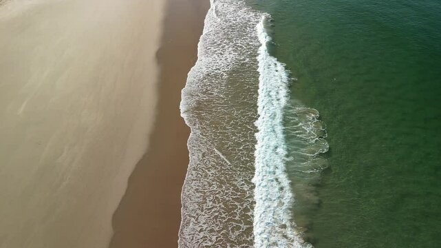 Aerial view over an empty sand beach with Atlantic ocean's waves in the small town Trafaria, Lisbon