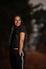 A Brazilian woman in a black outfit, smiling brightly, stands with hands in her pockets